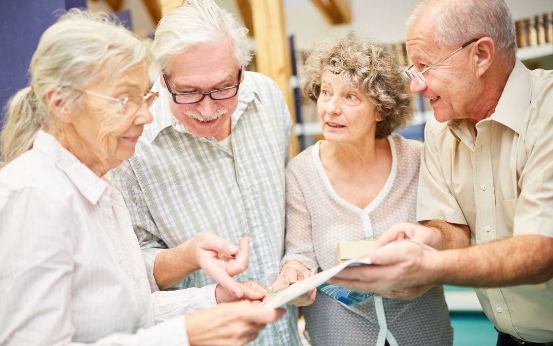 Sprachkenntnis in der 24-Stunden-Betreuung Betreuungskraft spricht ruhig mit einem Senior im Wohnzimmer und erklärt den nächsten Schritt im Alltag